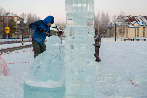 The sculptor cuts an ice figure out of a block of ice for Christmas