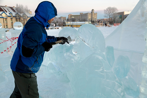 The sculptor cuts an ice figure out of ice with a chisel for Christmas