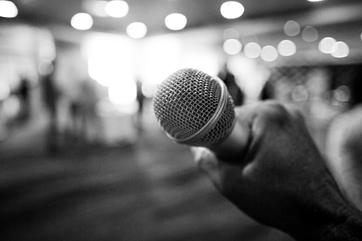 A person holds a microphone infront of out of focus people