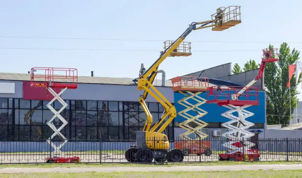 Photo of Different scissor and articulated boom wheeled lifts against industrial building