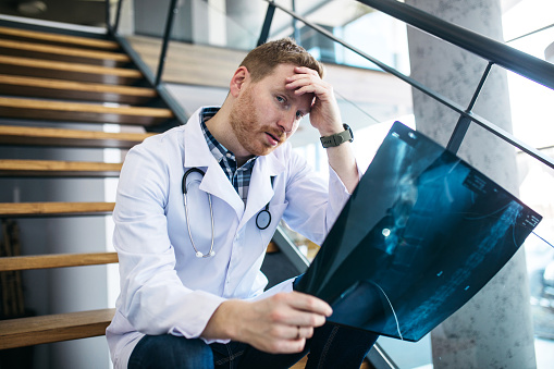 Young exhausted and frustrated doctor sitting depressed in the modern clinic on the stairs.