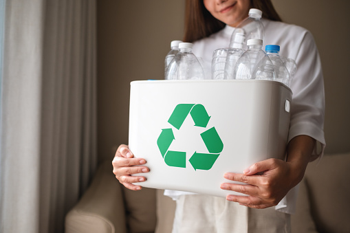 Closeup image of a woman collecting and separating recyclable garbage plastic bottles into a trash bin at home