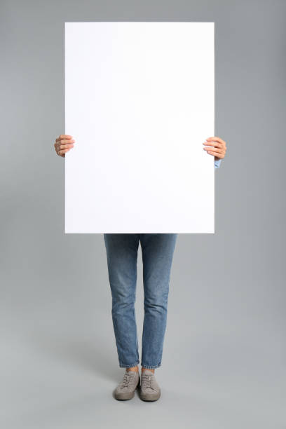 istock Woman holding white blank poster on grey background. Mockup for design 1370667828