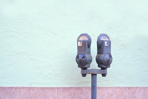 Two old metal parking meters, with a slot for coins, stand outdoors in front of a green plastered wall. There is space for text.
