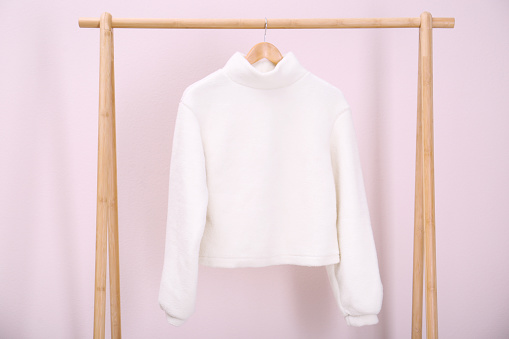 Stylish knitted sweater hanging on clothing rack near pink wall