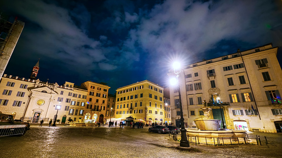 A suggestive night view of Piazza Farnese (Farnese Square), near Campo de Fiori, with on the right a fountain built in 1626 by the architect Girolamo Rainaldi, some ancient palaces and on the left the church of Santa Brigida (St Bridget of Sweden). The Piazza Farnese district is an area of the Eternal City much loved and visited by tourists and residents for the presence of ancient churches and noble palaces and for the countless artistic and cultural treasures of the Renaissance and Baroque era. Around the square, in the ancient Rione Regola (Regola district), you can explore dozens of characteristic alleys, with restaurant and bistrot, where you can discover the essence and soul of Roman life. In 1980 the historic center of Rome was declared a World Heritage Site by Unesco. Super wide angle image in high definition and 16:9 format.