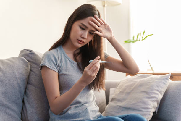 istock Young Asian woman measuring her temperature with a thermometer. 1370672116