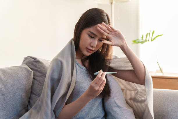 istock Young Asian woman measuring her temperature with a thermometer. 1370672160