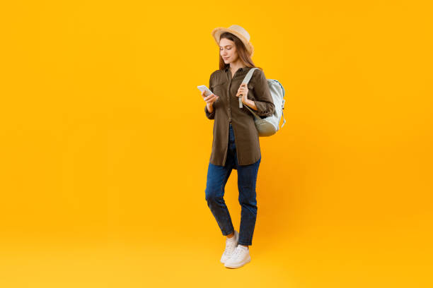 istock Tourist Lady Using Smartphone Browsing Internet Holding Backpack, Yellow Background 1370672171