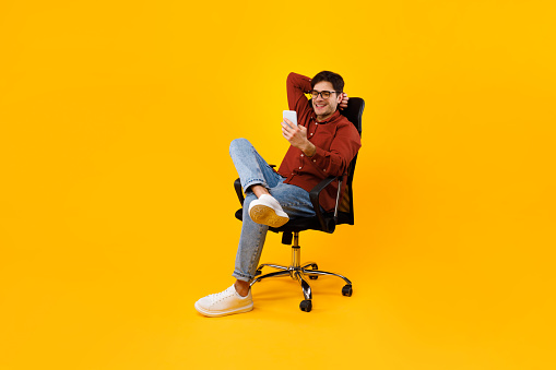 Hombre usando un teléfono inteligente sentado en la silla enviando mensajes de texto sobre fondo amarillo photo