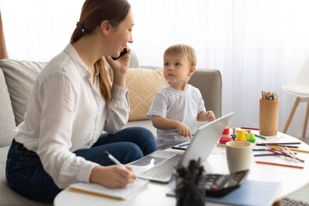 istock Young busy mother working from home with kid, talking on cellphone and making notes in notepad 1370672272