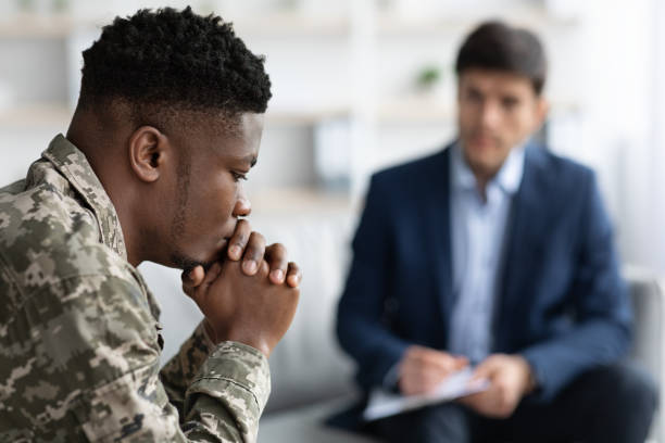 Pensive black soldier having conversation with social worker Pensive black man in camouflage uniform soldier having conversation with social worker, selective focus on african american military guy suffering from PTSD after returning home, blurred background post traumatic stress disorder photos stock pictures, royalty-free photos & images