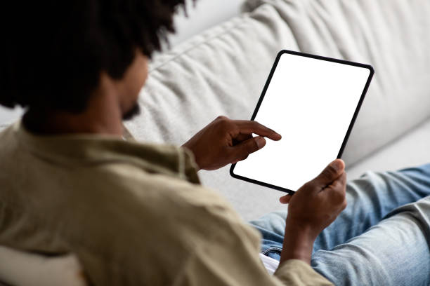 junger schwarzer mann mit leerem digitalen tablet mit weißem bildschirm zu hause - white tablet stock-fotos und bilder