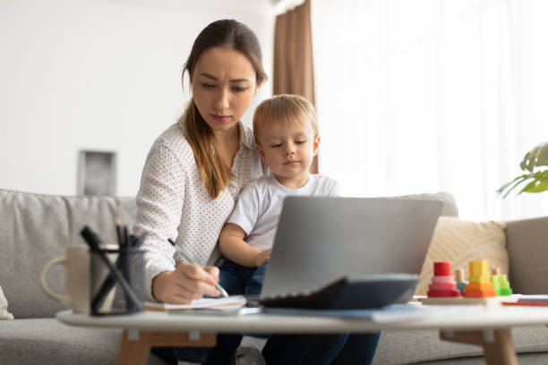 istock Distance learning. Young lady with child studying online, watching webinar and writing notes in notepad 1370672803