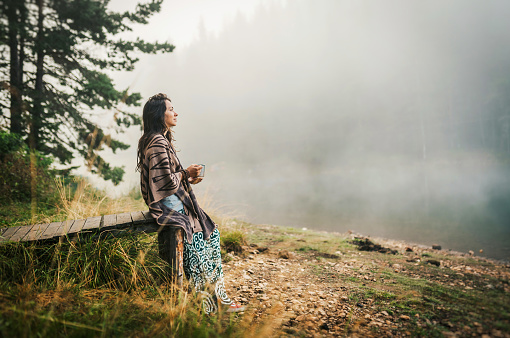 Portrait of a hippie woman sitting near a foggy lake.