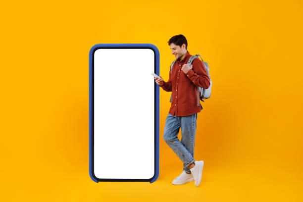 istock Traveler Guy Using Phone Standing Near Big Cellphone, Yellow Background 1370674131