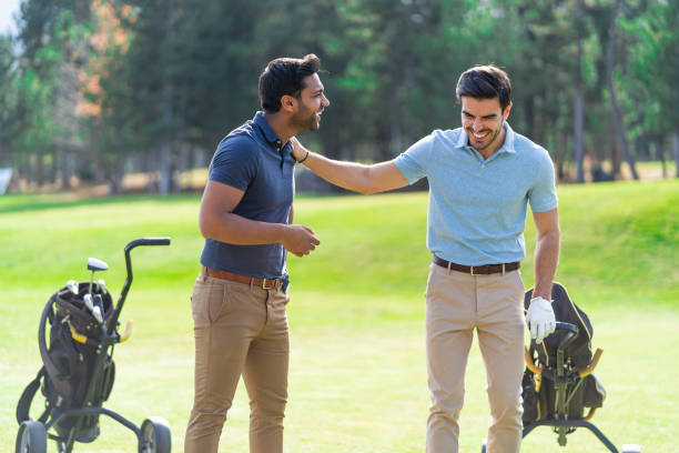 istock Smiling young golf players standing next to wheeled golf bags on the golf course  while discussing and laughing 1370683572
