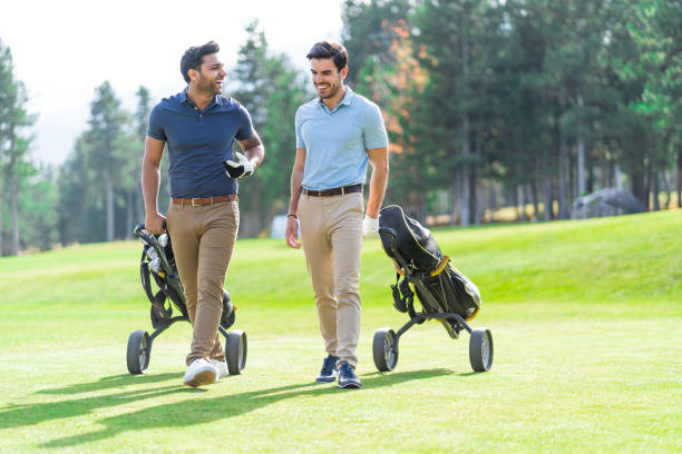 istock Smiling young golf players holding golf clubs and pulling their wheeled golf bags while talking on a golf course. 1370683574