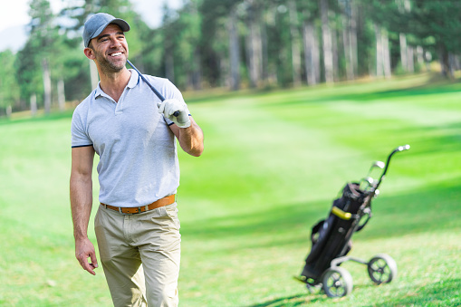 Adult golf player standing leisurely on the golf course and looking away to the goal