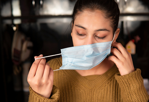 Young woman removing surgical protective face mask and for taking a deep breath and relaxed herself at home during coronavirus COVID-19, pandemic.