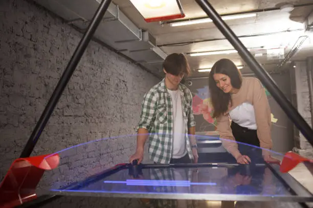 Happy young people laughing, playing air hockey together, copy space