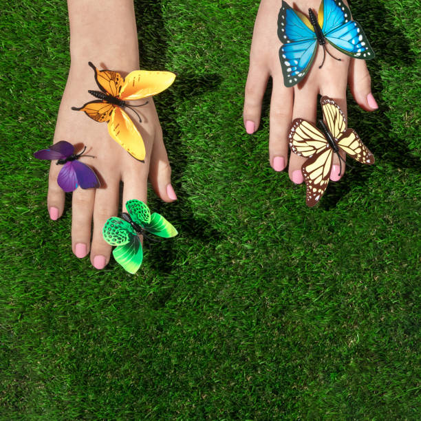 istock Spring creative layout with multi colored butterflies on hands against bright green grass background. Romantic fashion aesthetic concept. Minimal summer idea. 1370686328