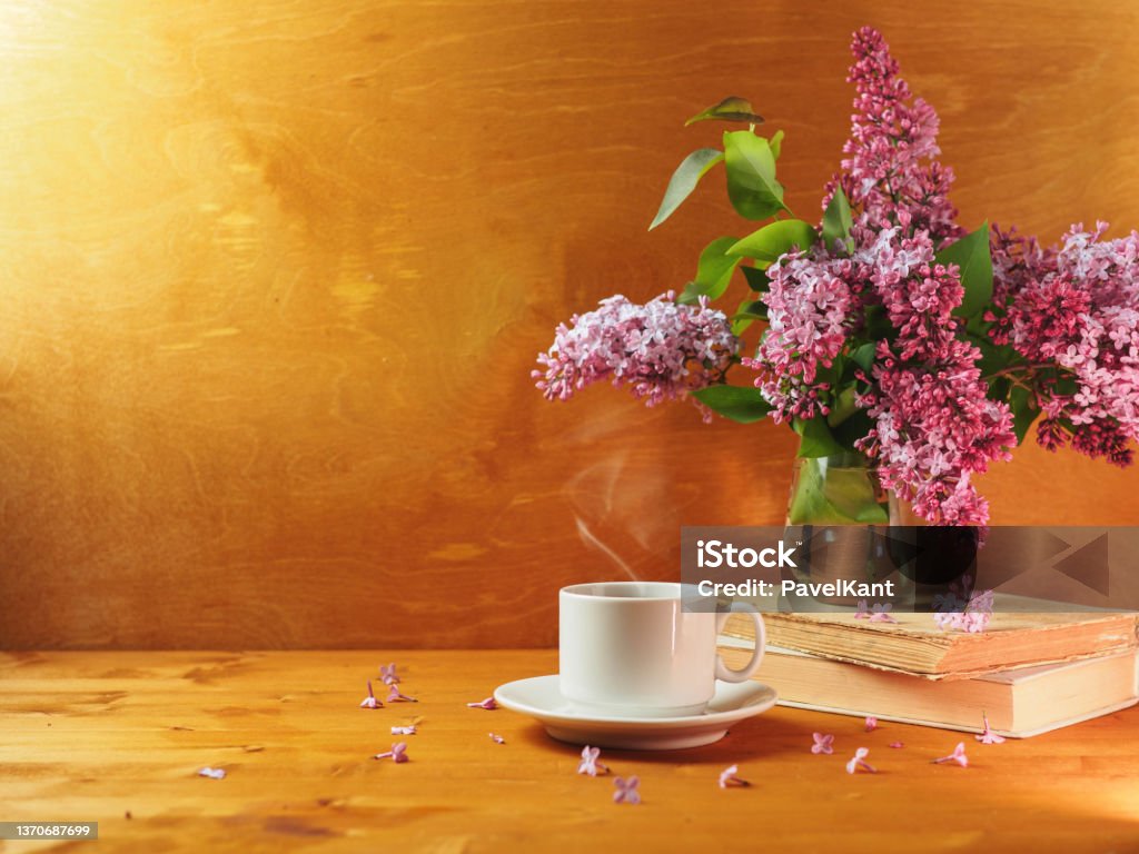 A cup of hot coffee or tea on a wooden table and a vase with a bouquet of lilac. Copy space A cup of hot coffee or tea on a wooden table and a vase with a bouquet of lilac Tea - Hot Drink Stock Photo