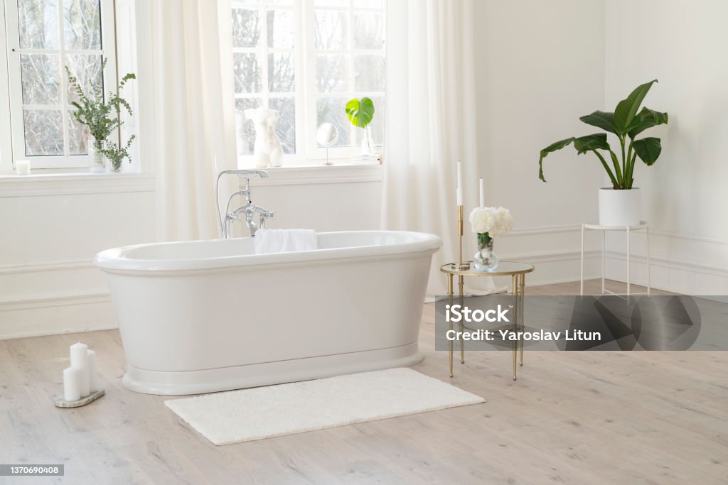 White modern bathroom with silver fittings with large sunny windows, decorations and plants. Interior design concept. Soft selective focus. White modern bathroom with silver fittings with large sunny windows, decorations and plants. Interior design concept. Soft selective focus Bathtub Stock Photo