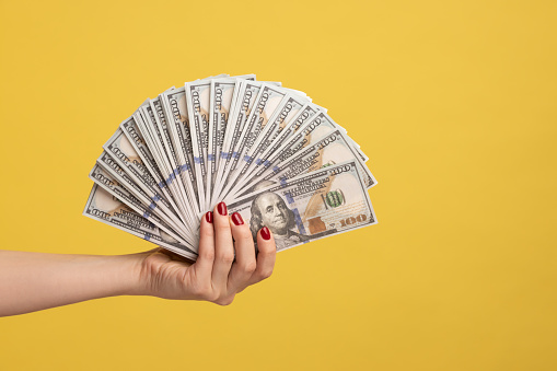 Vista lateral en primer plano de la mano de la mujer que muestra el ventilador de los billetes de dólar, el brazo sosteniendo efectivo, mucho dinero. photo