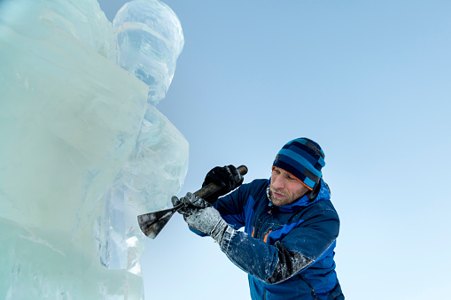 The sculptor cuts an ice figure out of ice with a chisel for Christmas