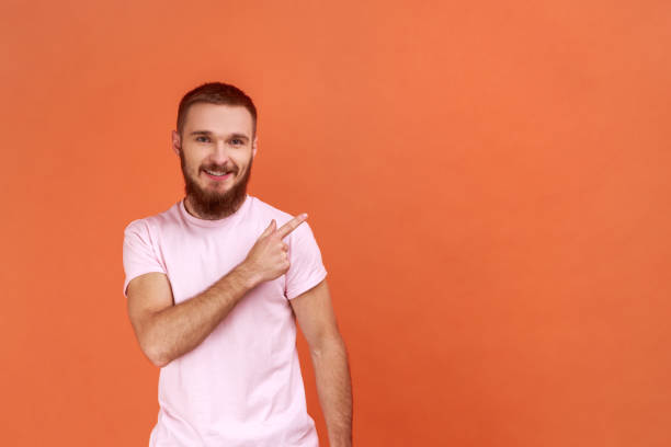 istock Man standing, looking at camera with happy positive face and pointing at wall copyspace. 1370692161