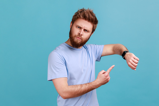 Man In Blue Tshirt Pointing Finger On His Wristwatch Impatiently Man In Blue Tshirt Pointing Finger On His Wristwatch Impatiently