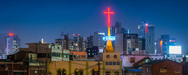 Neon red cross glowing over the rooftops and the crowded highrise cityscape of central Seoul at night, South Korea.