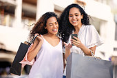 Shot of two young friends using a mobile phone during a shopping trip