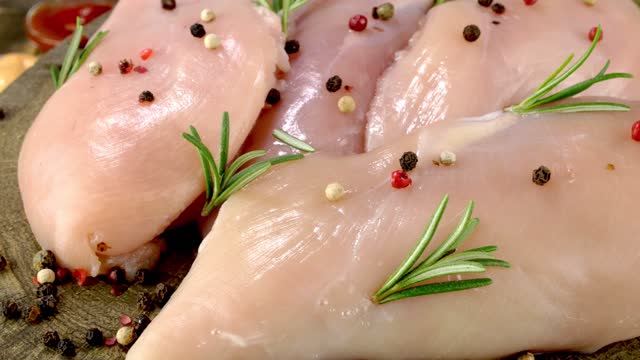 Fresh raw chicken breast fillets sprinkled with peppercorns and rosemary rotates slowly.