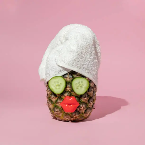 Creative concept with pineapple, towel turban or wrap,slices of cucumber and bright red lips on pastel pink background. Happy fun girl life idea. Surreal fashion or cosmetic composition.
