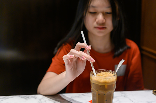 Asian Chinese girl stirring a glass of iced coffee