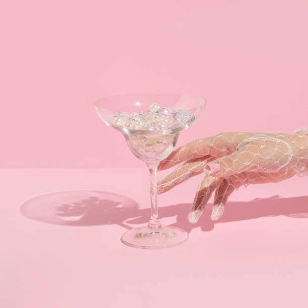 istock Creative layout with hand in white lace glove  raeching martini cocktail glass with diamonds and pearls on pastel pink background. 80s or 90s retro aesthetic fashion concept. Romantic drink idea. 1370698570