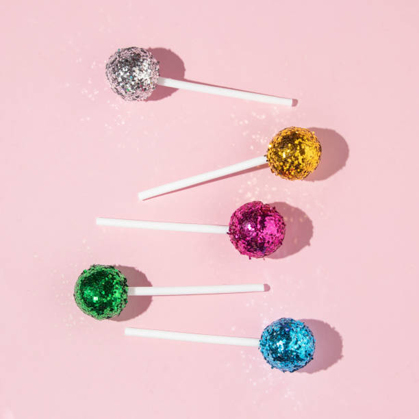 Creative colorful flat lay with lollipops and bright pink,yellow,green,blue and silver glitter on pastel pink background. Party fun happy life idea with lollipop or candy. Minimal flat lay.