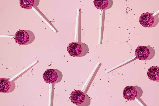 istock Creative pattern with lollipops and bright pink glitter on pastel pink background. Party fun happy life concept. Minimal flat lay with candy. 1370700577