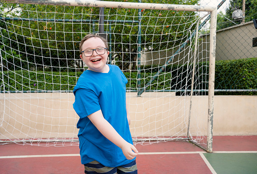 Boy with down syndrome playing with ball at sports court in a sunny day
