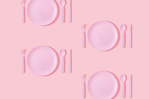 Creative pattern made with pastel pink plate, spoon, fork and knife on pastel pink background. Minimal surreal breakfast idea or food restaurant concept. Vintage aesthetic 80s or 90s fashion background.