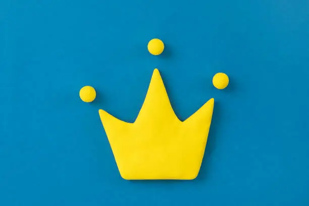 Photo of Simple 3d yellow crown symbol on blue background. Concept of win and success, top rank quality status.