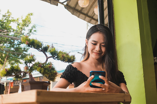 Una joven asiática feliz que está ocupada enviando mensajes de texto o chateando por teléfono. En una cafetería al aire libre. photo