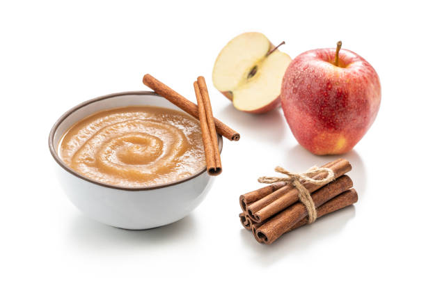Apple sauce or apple pureed compote homemade with raw red apples on white background and cinnamon sticks