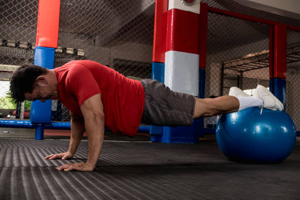 A muscular and fit asian man does pushups on a stability ball. Abdominal and core exercise and workout. Overhead shot.