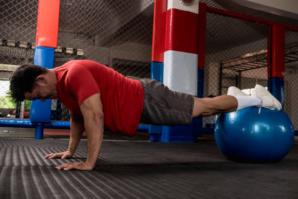 A muscular and fit asian man does pushups on a stability ball. Abdominal and core exercise and workout. Overhead shot. A muscular and fit asian man does pushups on a stability ball. Abdominal and core exercise and workout. Overhead shot. PUSH UP stock pictures, royalty-free photos & images