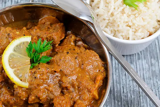 Indian curry garnished with lemon with rice on slate.