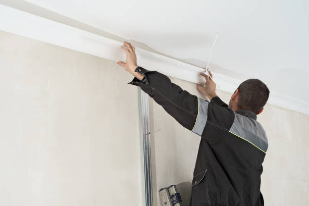 Installation of ceiling detail of corner crown molding. Worker fixes the plastic molding to the ceiling. stock photo