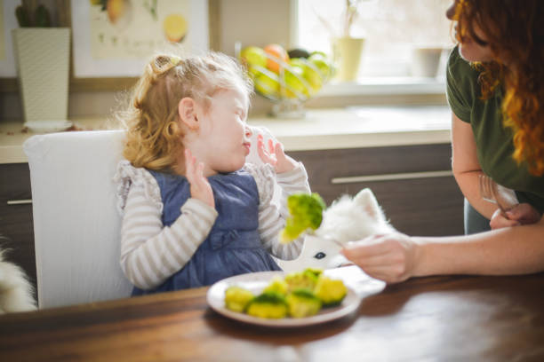 母と赤ちゃんの女の子のブロンドホームのインテリアで、ブロッコリーを食べる - baby child babies only baby girls ストックフォトと画像